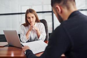 chico sentado con documentos. mujer y hombre con ropa formal trabajando juntos en el interior de la oficina junto a la mesa foto