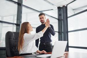 Woman and man in formal clothes giving high five to each other indoors in the office photo