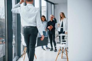 Man in formal clothes walking and talking. Group of young successful team that working and communicating together indoors in office photo