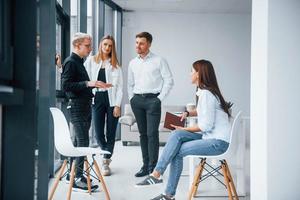 Group of young positive team have work and communicating together indoors in office near windows photo