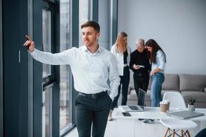 Man in formal clothes standing in front of young successful team that working and communicating together indoors in office photo