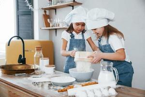 Two little girls in blue chef uniform working with flour by using sieve on the kitchen photo