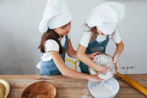 dos niñas con uniforme de chef azul trabajando con harina en la cocina foto