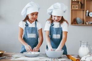 dos niñas con uniforme de chef azul trabajando con harina en la cocina foto