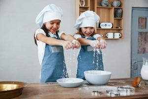 dos niñas con uniforme de chef azul trabajando con harina en la cocina foto