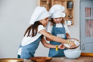 Two little girls in blue chef uniform working with flour on the kitchen photo