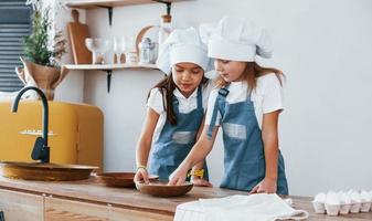 dos niñas con uniforme de chef azul trabajando con harina en la cocina foto