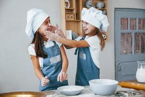 Two little girls in blue chef uniform have fun with flour on the kitchen photo