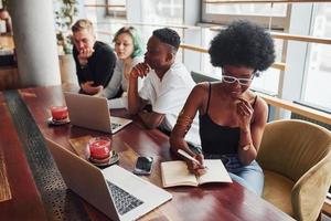 Black woman sitting in front of group of multi ethnic people with alternative girl with green hair is working together by the table indoors photo