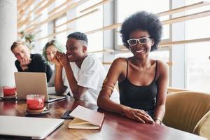 Black woman sitting in front of group of multi ethnic people with alternative girl with green hair is working together by the table indoors photo