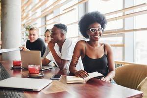 Black woman sitting in front of group of multi ethnic people with alternative girl with green hair is working together by the table indoors photo