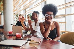 Black woman sitting in front of group of multi ethnic people with alternative girl with green hair is working together by the table indoors photo