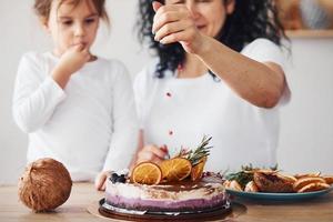 Senior woman with her granddaughter preparing dietical cake on kitchen photo