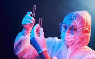 Nurse in mask and white uniform standing in neon lighted room and holding tubes with samples photo