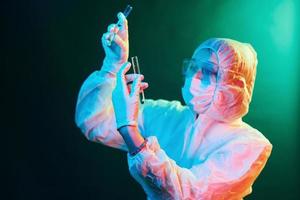 Nurse in mask and white uniform standing in neon lighted room and holding tubes with samples photo