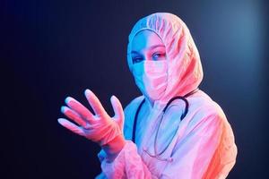 Nurse in mask and white uniform standing in neon lighted room photo