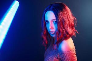 retrato de una joven con el pelo rizado que sostiene palos de luz en neón rojo y azul en el estudio foto