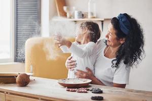 Senior woman with her granddaughter preparing food with flour on kitchen and have fun photo