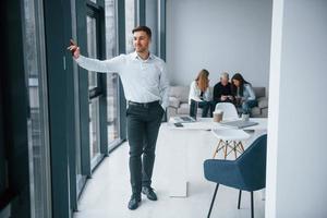 Man in formal clothes standing in front of young successful team that working and communicating together indoors in office photo