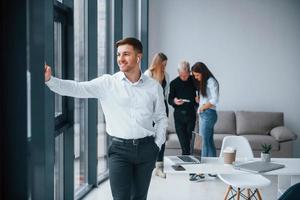 Man in formal clothes standing in front of young successful team that working and communicating together indoors in office photo