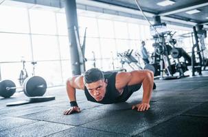 Strong young man in sportive clothes doing push ups in gym photo