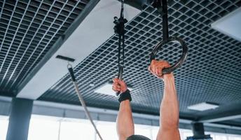 joven fuerte con ropa deportiva haciendo ejercicios en anillos de gimnasia en el gimnasio foto