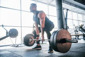 Strong young man in sportive clothes doing exercises with heavy weights in the gym photo