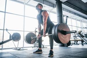 Strong young man in sportive clothes doing exercises with heavy weights in the gym photo