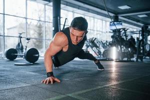 Strong young man in sportive clothes doing push ups in gym photo