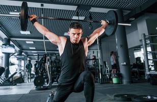 joven fuerte con ropa deportiva haciendo ejercicios con pesos pesados en el gimnasio foto