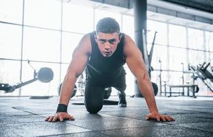 Strong young man in sportive clothes doing push ups in gym photo