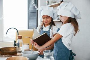 Two little girls in blue chef uniform preparing food on the kitchen and reading receipt book photo