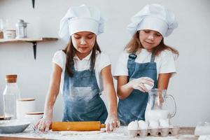 dos niñas con uniforme de chef azul amasando masa en la cocina