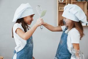 dos niñas pequeñas con uniforme de chef azul preparando comida en la cocina foto