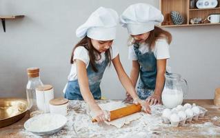 dos niñas con uniforme de chef azul amasando masa en la cocina foto