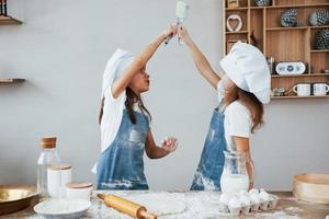 Two little girls in blue chef uniform kneading dough on the kitchen photo