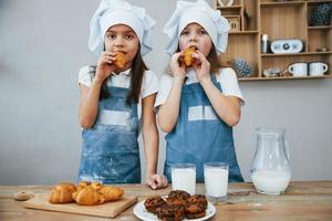 dos niñas con uniforme de chef azul comiendo comida en la cocina foto