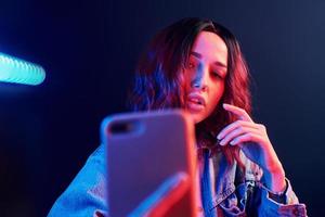 Portrait of young girl with curly hair that makes selfie by using phone in red and blue neon in studio photo