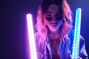 Portrait of young girl in glasses holding light sticks in red and blue neon in studio photo