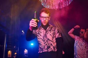 Guy in glasses drinks beer. Young people is having fun in night club with colorful laser lights photo