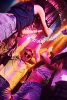 View from below of young people that having fun in night club with colorful laser lights photo