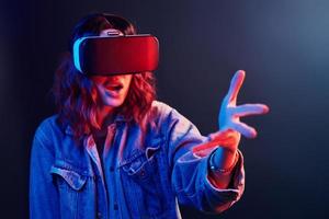 expresión facial de una joven con gafas de realidad virtual en la cabeza en neón rojo y azul en el estudio foto
