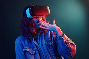 Facial expression of young girl with virtual reality glasses on head in red and blue neon in studio photo