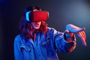 Facial expression of young girl with virtual reality glasses on head in red and blue neon in studio photo