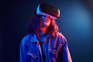 Facial expression of young girl with virtual reality glasses on head in red and blue neon in studio photo