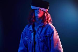 Facial expression of young girl with virtual reality glasses on head in red and blue neon in studio photo