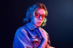 Portrait of young alternative girl in glasses with green hair in red and blue neon light in studio photo