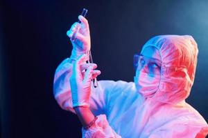 Nurse in mask and white uniform standing in neon lighted room and holding tubes with samples photo