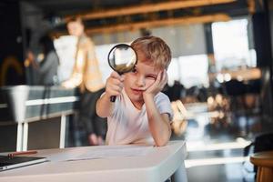 Smart child in casual clothes with laptop on table have fun with magnifying glass photo