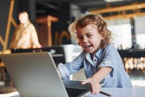 Smart child in casual clothes using laptop for education purposes or fun photo